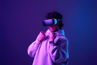 man in sweatshirt using virtual reality headset on blue background. Neon lighting