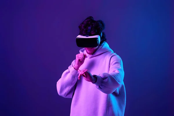 Stock image man in sweatshirt using virtual reality glasses and playing video games on blue background. Neon lighting