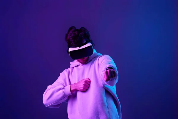 stock image man in sweatshirt using virtual reality glasses on blue background. Neon lighting