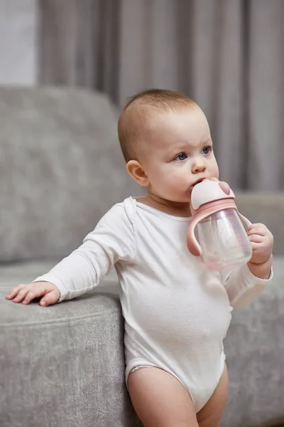 可爱的女婴在家里抱着瓶子喝水 — 图库照片