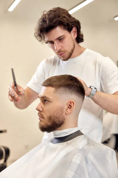 在理发店里 专业理发师用梳子和剪刀为高加索男人理发 — 图库照片