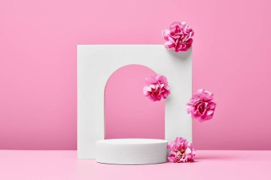 Pembe çiçekli beyaz podyum ve pastel pembe arka planda izole edilmiş zarif kemer. sunum için sahne kozmetik ürünleri