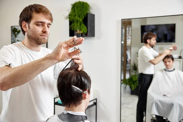若いです白人男性取得散髪によってプロの男性美容師使用櫛と身づくろいはさみで現代の白い理容師店 — ストック写真