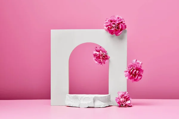 パステルピンクの背景にピンクの花 石とエレガントなアーチを持つ白の表彰台 化粧品の発表段階 — ストック写真