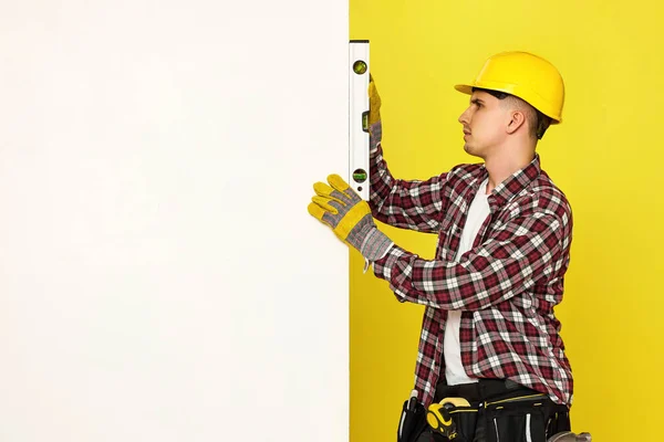 professional builder in work clothes in helmet using spirit level and measuring vertical surface. copy space for text