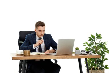 İş yerinde dizüstü bilgisayara bakarken çevrimiçi projeyi düşünen yakışıklı bir adam.