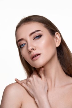 Güzel, harika, genç bir kadın omzuna dokunuyor ve beyaz arka planda kusursuz, yumuşak, temiz bir tenin tadını çıkarıyor.