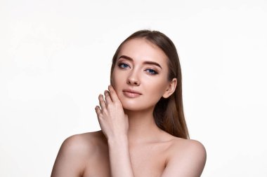 Güzel genç bir kadın yanaklara dokunuyor ve beyaz arka planda mükemmel tenin tadını çıkarıyor.