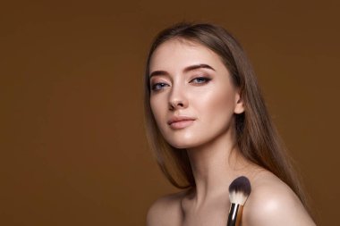 Bej arka planda makyaj fırçasıyla yanaklarına allık süren genç bir kadın. Boşluğu kopyala