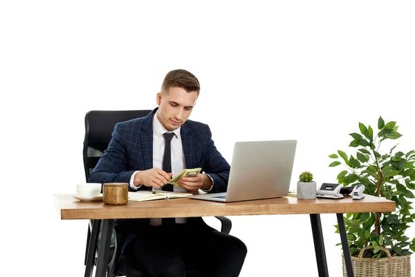 若いビジネスマンがノートパソコンで働いてお金を持って机の上で椅子に座って — ストック写真