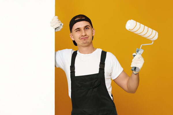 young man in working clothes painting white walls in the room. copy space for text