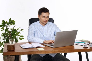 Genç adam, beyaz arka plandaki masada online iş için dizüstü bilgisayar kullanıyor.