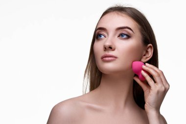 Beyaz arka planda pembe kozmetik süngerler kullanan çekici genç bir kadın. Boşluğu kopyala