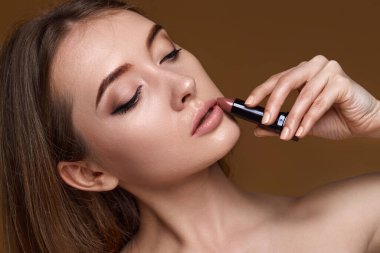 Bej arka planda çıplak pembe ruj tutan güzel, gülümseyen bir kadın.