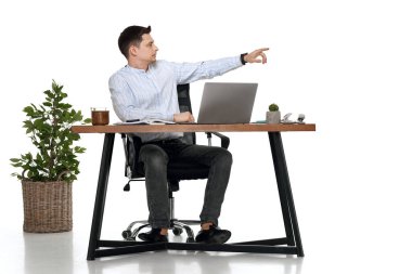 Genç adam masada çalışmak için dizüstü bilgisayar kullanıyor ve beyaz arkaplandaki kopyalama alanına işaret ediyor