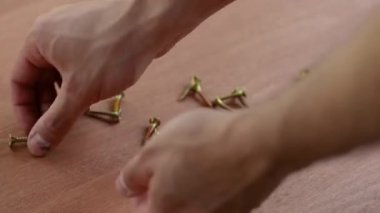 Erkek eli tahta masada vida topluyor. İşçi vida alır