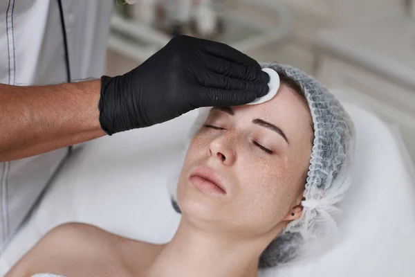 beautician cleanses skin of beautiful woman with cotton sponge. Perfect cleaning, spa treatment skincare face.