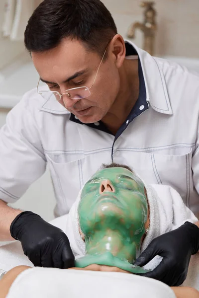 Mannelijke Schoonheidsspecialiste Verwijderen Groene Alginaat Masker Van Gezicht Van Mooie — Stockfoto