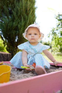 Kum havuzunda oynayan sevimli küçük kız dışarıda oyun alanında çeşitli oyuncaklar var.