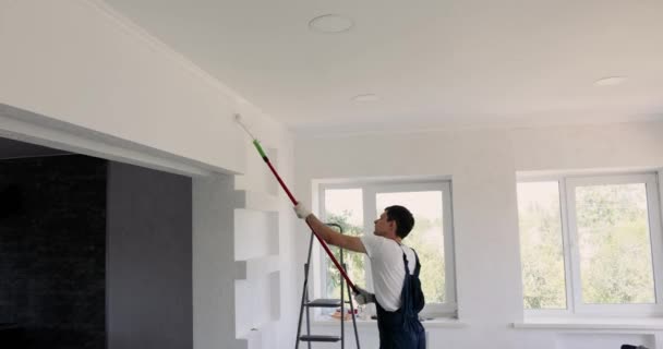 蓝色工作服的修理工在装修房间时 是用白色的滚子粉刷墙壁的 油漆工 — 图库视频影像