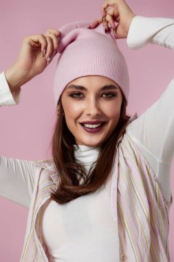 Mutlu kadın portresi, ellerini pembe arka planda pembe şapkanın üzerinde tutuyor..