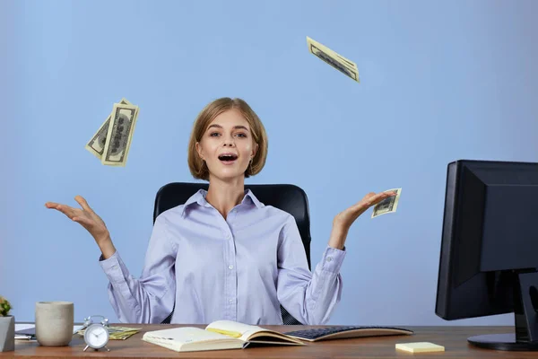 successful businesswoman throwing money while sitting on chair at desk. banknotes fly in the air