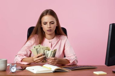 Başarılı bir iş kadınının pembe arka planda sandalyede otururken elinde para tutması tatmin edici.