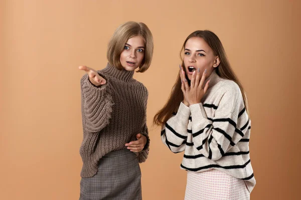 Two women friends together in casual clothes point index finger aside on beige background. Surprised blonde woman and her friend