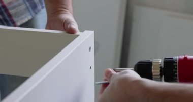 Marangoz elektrikli tornavida kullanarak beyaz mobilya parçalarını düzüyor.