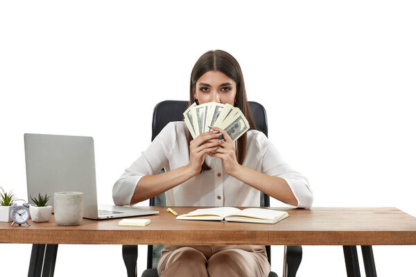 beautiful businesswoman working on laptop and holding money while sitting on chair at desk.