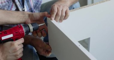 Marangoz elektrikli tornavida kullanarak beyaz mobilya parçalarını düzüyor.