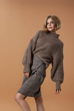 Kahverengi örgü süveterli güzel sarışın kadın bej arka planda poz veriyor. sonbahar biçimi