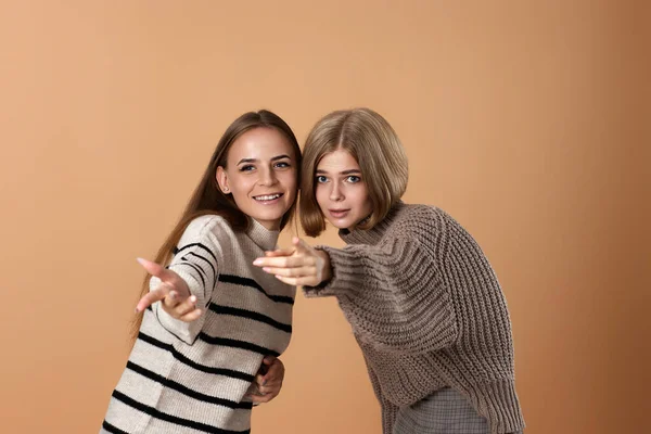 Two women friends together in casual clothes point index finger aside on beige background. Surprised blonde woman and her friend