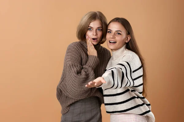 两个穿着休闲装的女性朋友把米色背景的食指放在一边 令人惊讶的金发女人和她的朋友 — 图库照片