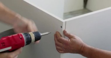 Marangoz elektrikli tornavida kullanarak beyaz mobilya parçalarını düzüyor.