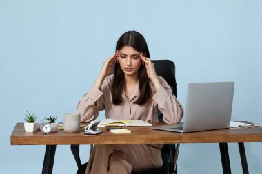 Ofiste dizüstü bilgisayar kullanan üzgün bir kadının başı ağrıyor.