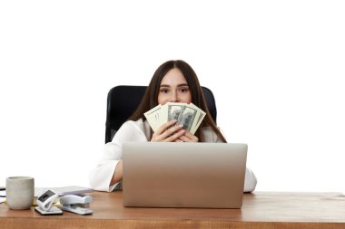 Mutlu iş kadını dizüstü bilgisayarda çalışıyor ve elinde para tutuyor.