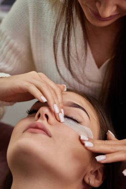 Kozmetik uzmanı göz altında yapıştırıcı şeridi hazırlıyor. Kirpik uzatma işlemi