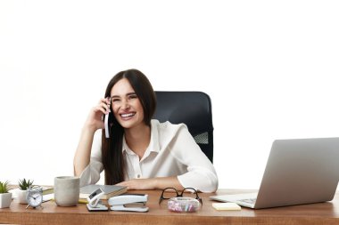 Güzel bir iş kadını laptopla çalışıyor ve ofiste telefon görüşmesi yapıyor.