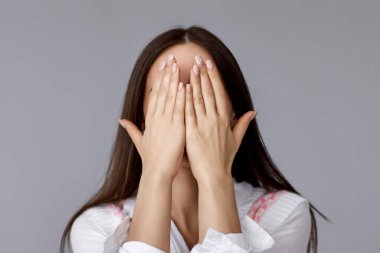 Gri arka planda sürpriz beklerken genç ve güzel bir kadın elleriyle gözlerini kapatıyor..