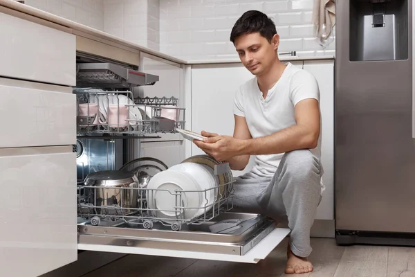 Красивый Позитивный Мужчина Вытаскивает Чистую Посуду Посудомоечной Машины Современной Белой — стоковое фото