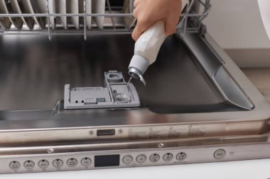 Kadın eli, modern beyaz mutfaktaki bulaşık makinesine deterjan döker.