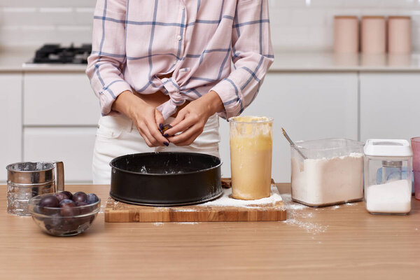 женские руки приготовления сливового пирога в светлом современном интерьере кухни.