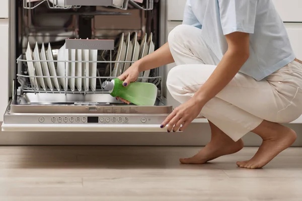 female hand pours rinse aid into the dishwasher compartment in modern white kitchen