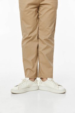 Stüdyo arka planında beyaz spor ayakkabı giyen ve günlük bej pantolon giyen bir adam.