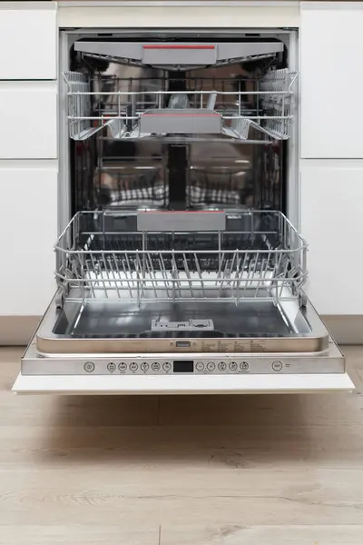 Modern built-in empty dishwasher with open door in the kitchen .