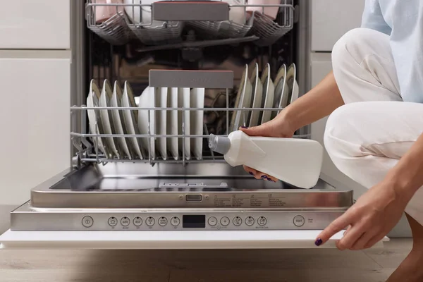 female hand pours rinse aid into the dishwasher compartment in modern white kitchen