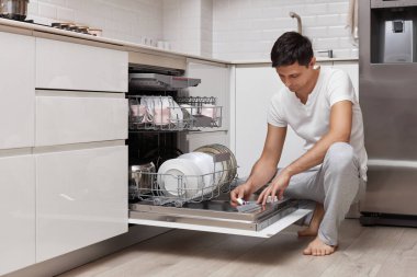 Yakışıklı adam bulaşık makinesine deterjan koyuyor.