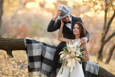 Güzel, mutlu, şık gelin ve damat sonbaharda ağaçların yanında şapka takıyor.