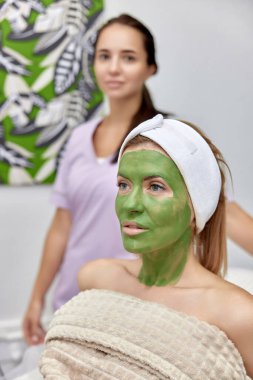 Kadın kozmetikçi ve kadın müşteri güzellik kliniğinde maske takıyor..